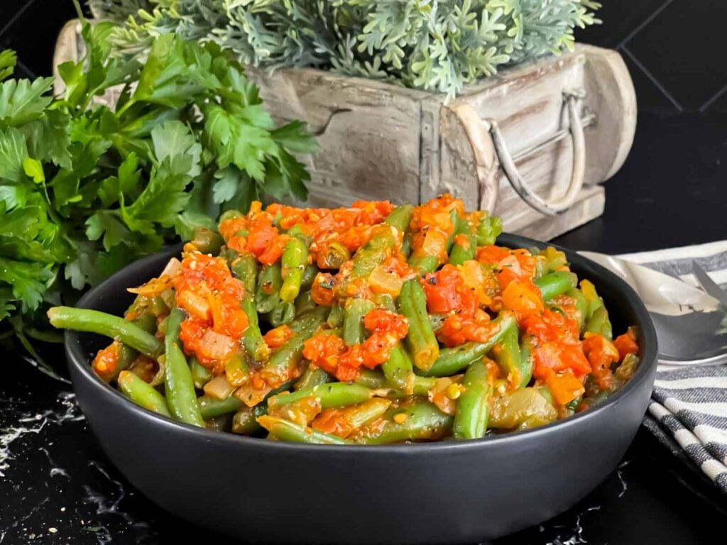 Green beans with tomato sauce in a dark bowl.