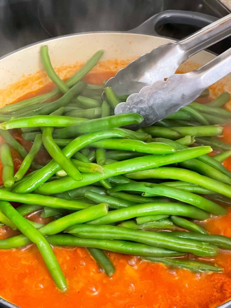 Adding green beans to tomato sauce.