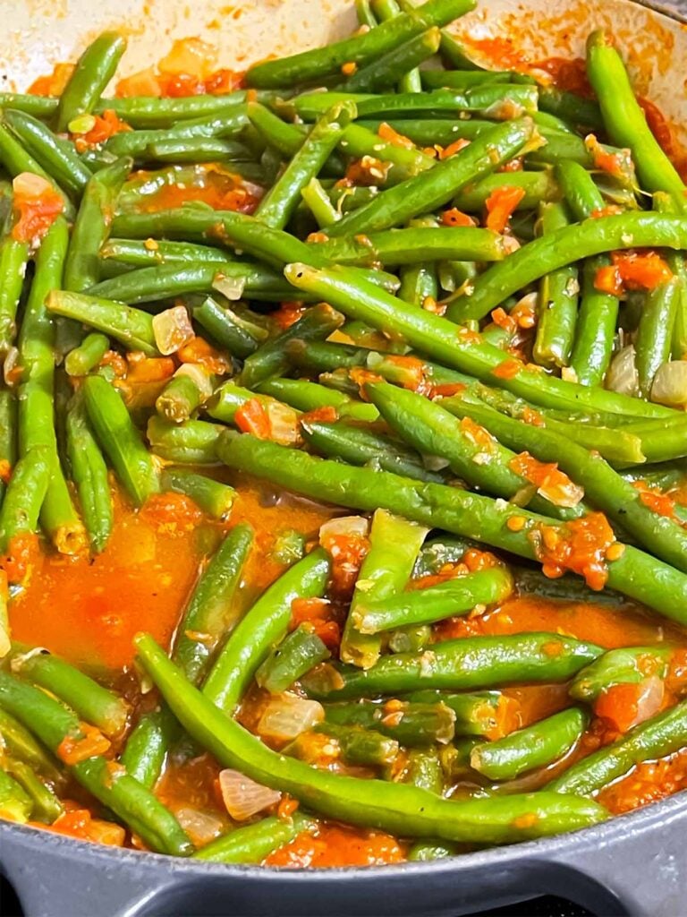 Green beans with tomato sauce cooking in a large skillet.