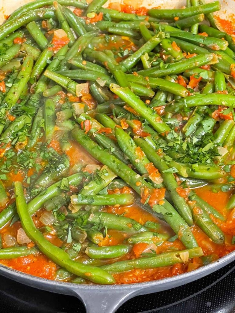 Green beans with tomato sauce cooking in a large skillet.