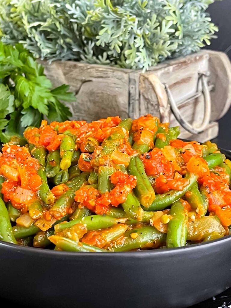 Green beans with tomato sauce in a dark bowl.