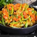 Green beans with tomato sauce in a dark bowl.