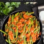 Green beans with tomato sauce in a dark bowl.
