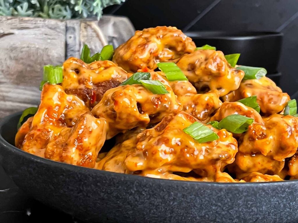 Bang Bang Chicken in a dark bowl, garnished with green onion.