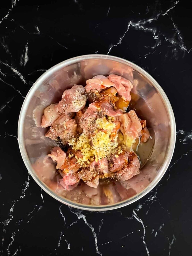 Bite sized pieces of chicken thigh in a bowl with spices on top.