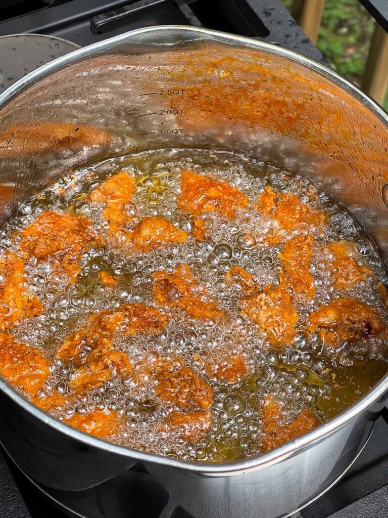 Bite sized chicken thigh pieces frying in oil.