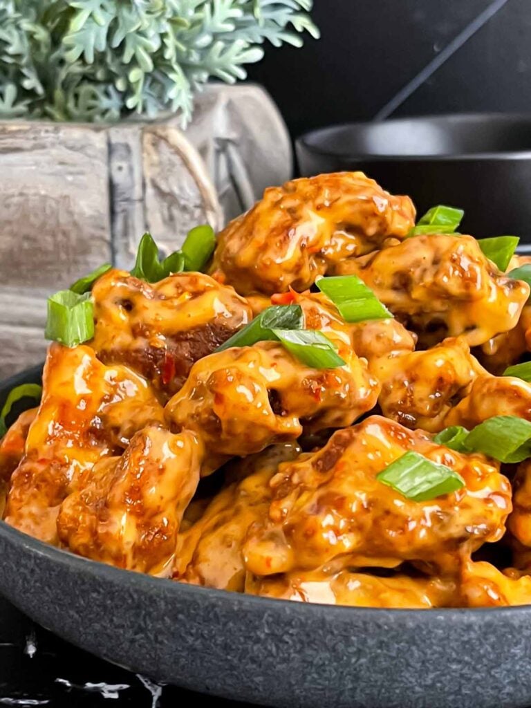 Bang Bang Chicken in a dark bowl, garnished with green onion.