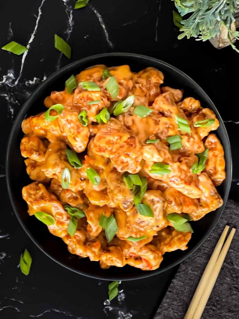 Bang Bang Chicken in a dark bowl, garnished with green onion.