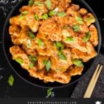 Bang Bang Chicken in a dark bowl, garnished with green onion.