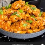 Bang Bang Chicken in a dark bowl, garnished with green onion.