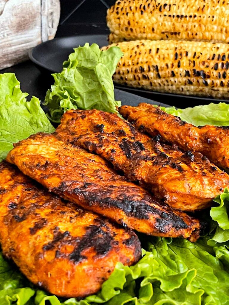 Grilled Southwest chicken on a bed of greens with grilled corn in the background.