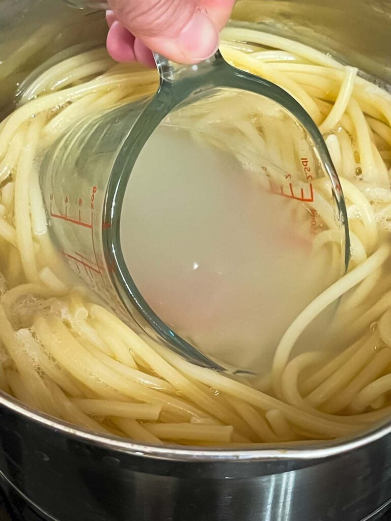 Removing pasta water using a measuring cup.