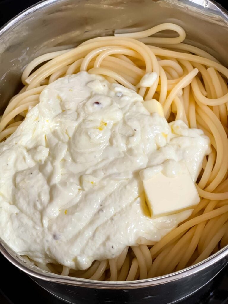 A lemon ricotta sauce being added to pasta in a cooking pot.