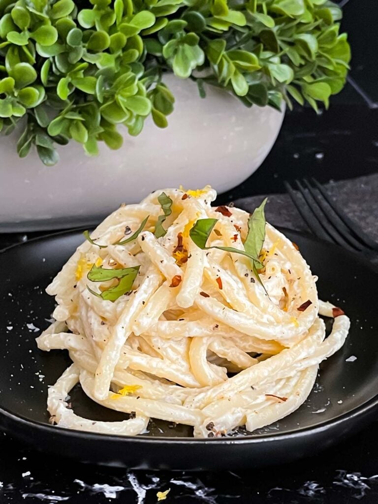 Lemon Ricotta Pasta, topped with black pepper and basil, on a dark plate.