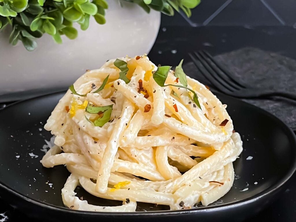 Lemon Ricotta pasta, topped with black pepper and basil, on a dark plate.