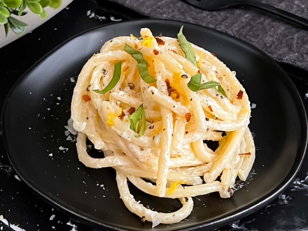 Lemon Ricotta pasta, topped with black pepper and basil, on a dark plate.