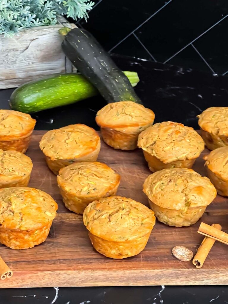 Zucchini muffins on a cutting board with some cinnamon sticks and nutmeg.