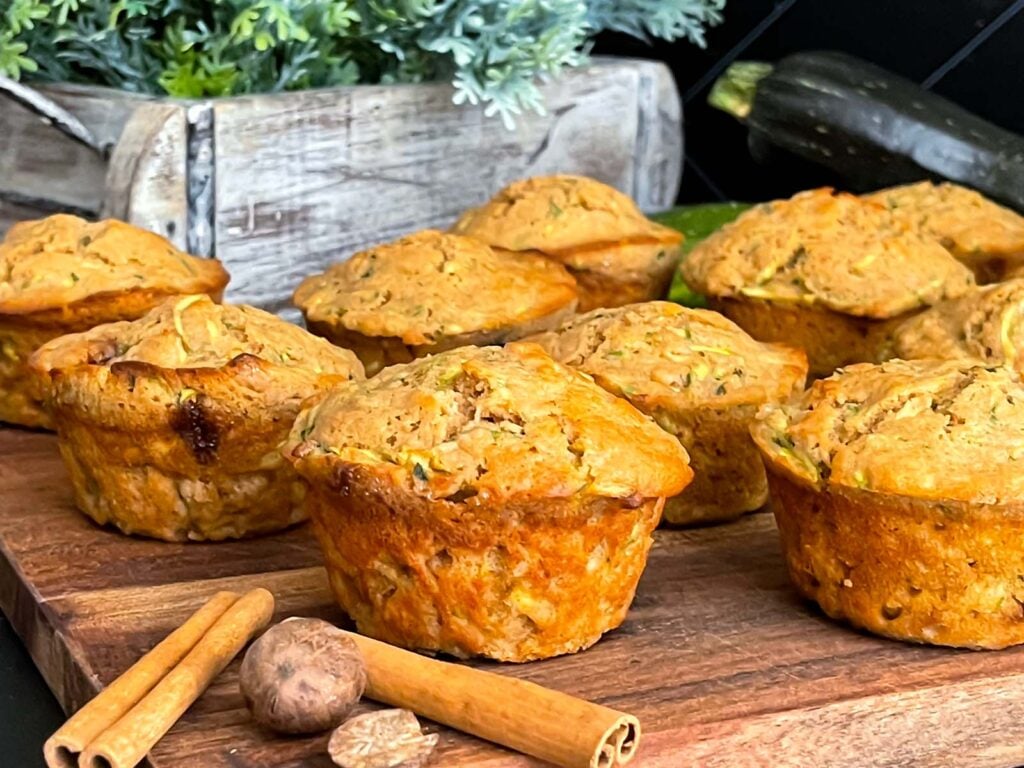 Zucchini muffins on a cutting board with some cinnamon sticks and nutmeg.