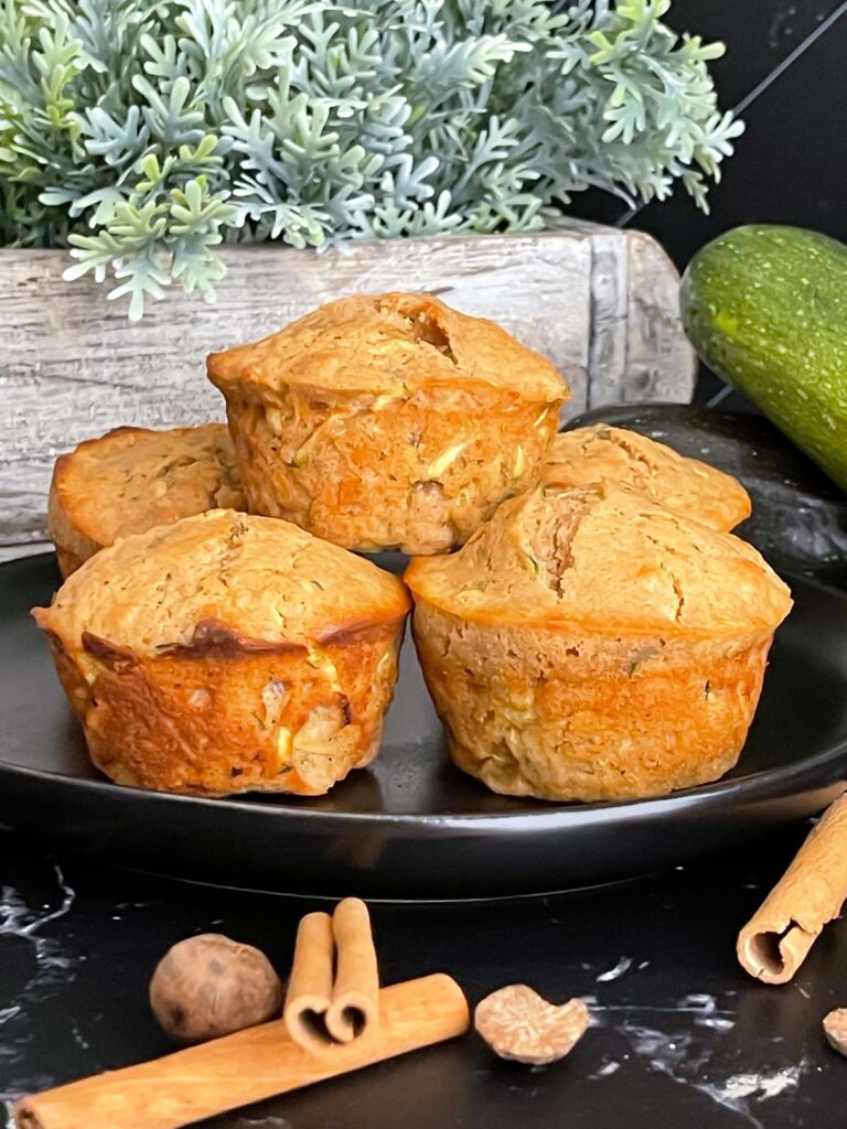 Zucchini muffins on a dark plate with some cinnamon sticks and nutmeg.