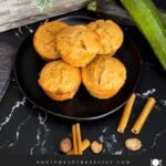 Zucchini muffins on a dark plate with some cinnamon sticks and nutmeg.