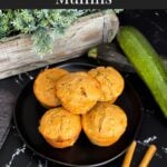 Zucchini muffins on a dark plate with some cinnamon sticks and nutmeg.