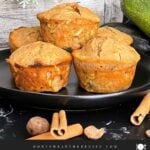 Zucchini muffins on a dark plate with some cinnamon sticks and nutmeg.