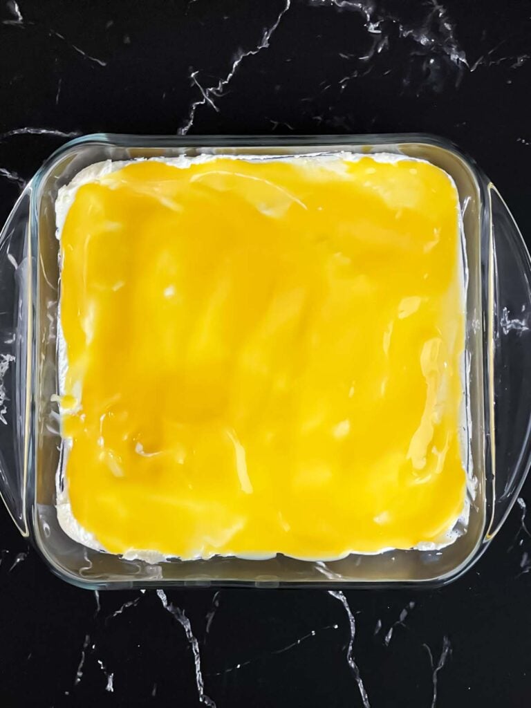 Lemon curd layered over the limoncello layer in a glass baking dish.