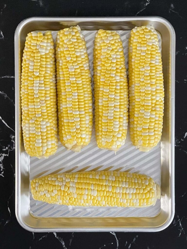 Corn on the cob on a small baking sheet.