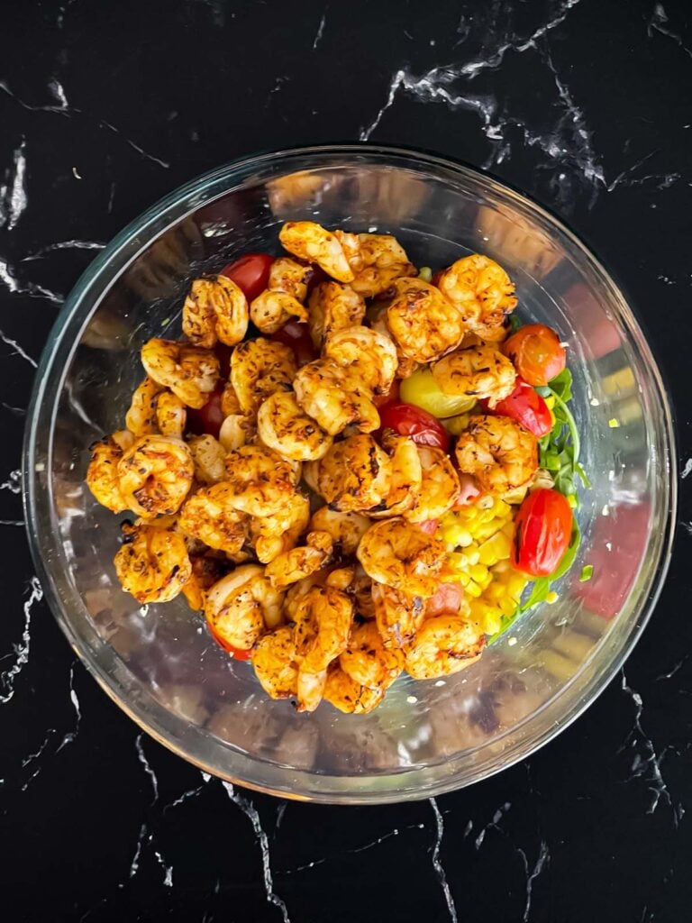 Shrimp on top of a salad in a glass bowl.