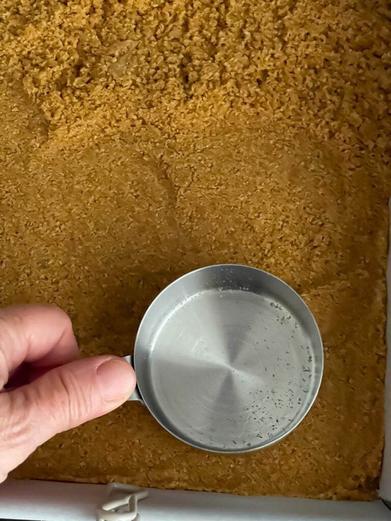 Pressing graham cracker crust into prepared pan.