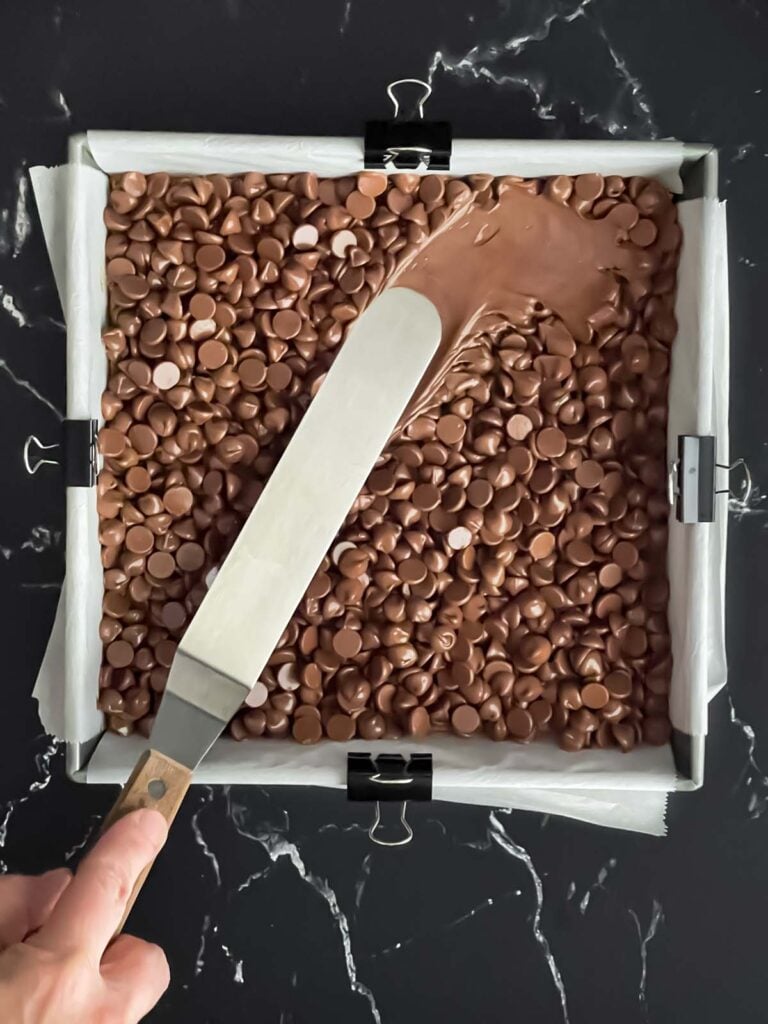 Spreading soft chocolate chips smooth over graham cracker crust.