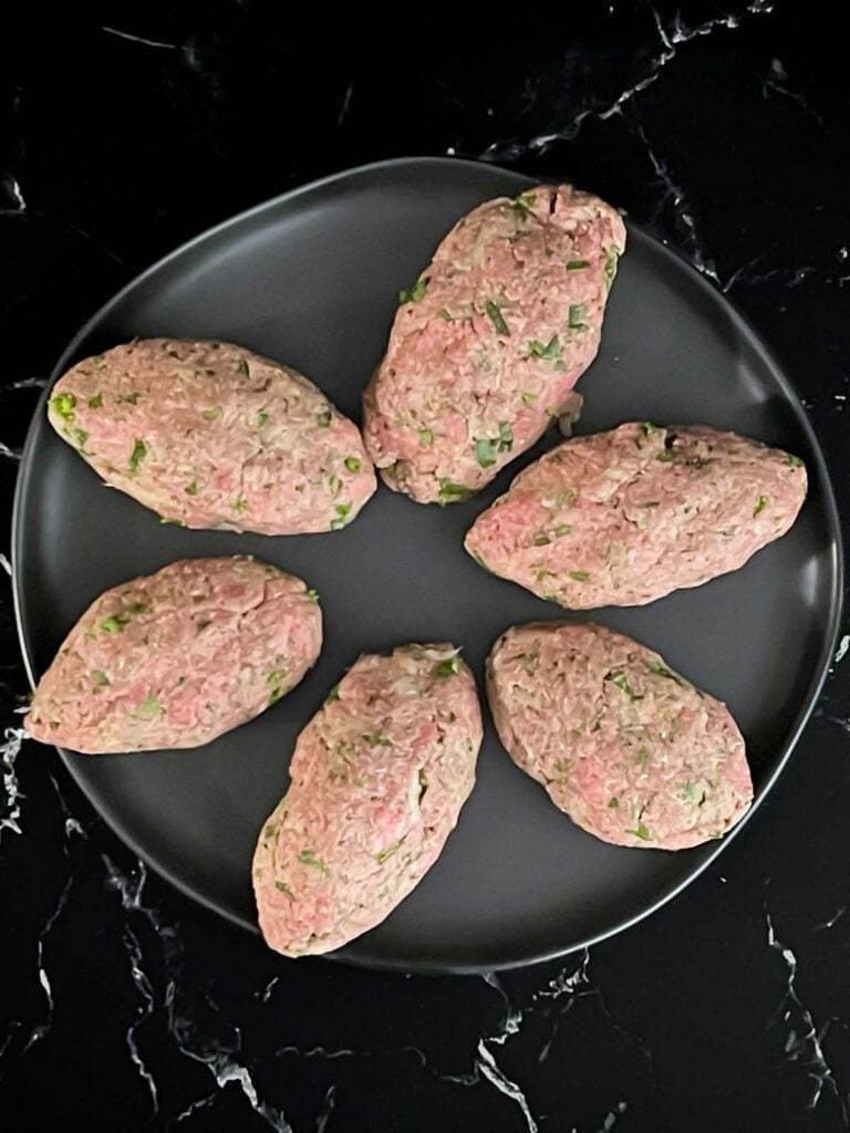 Kofte shaped into ovals on a black plate.