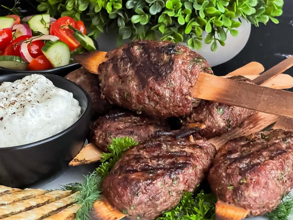 Spiced beef kebabs (kofte) with pita, tzatziki sauce, and a tomato cucumber salad.