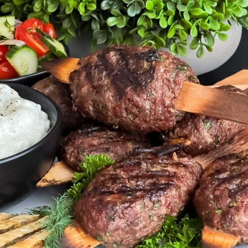Spiced beef kebabs (kofte) with pita, tzatziki sauce, and a tomato cucumber salad.
