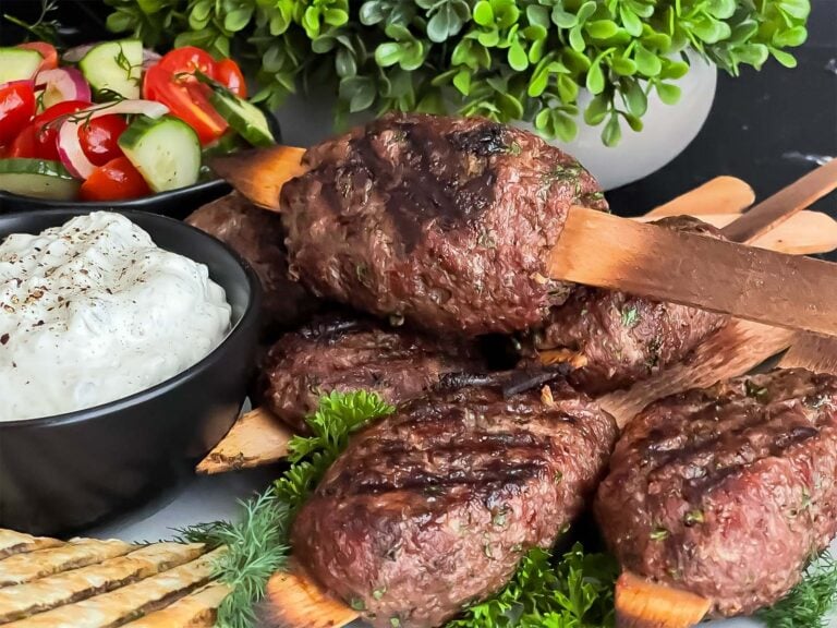 Spiced beef kebabs (kofte) with pita, tzatziki sauce, and a tomato cucumber salad.