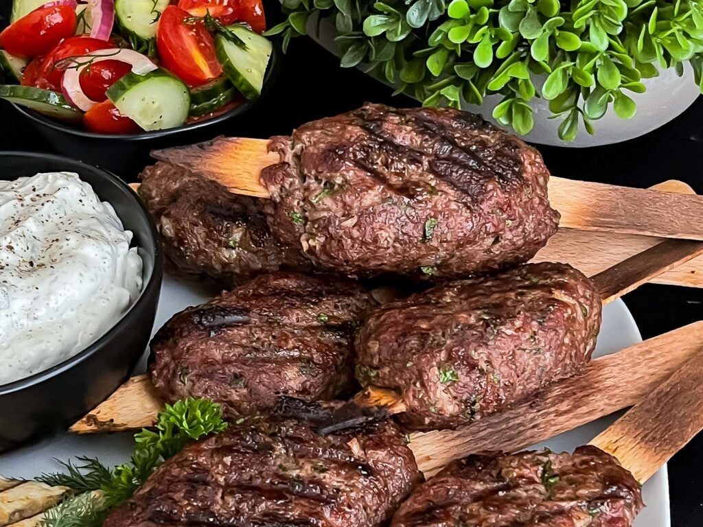 Spiced beef kebabs (kofte) with pita, tzatziki sauce, and a tomato cucumber salad.
