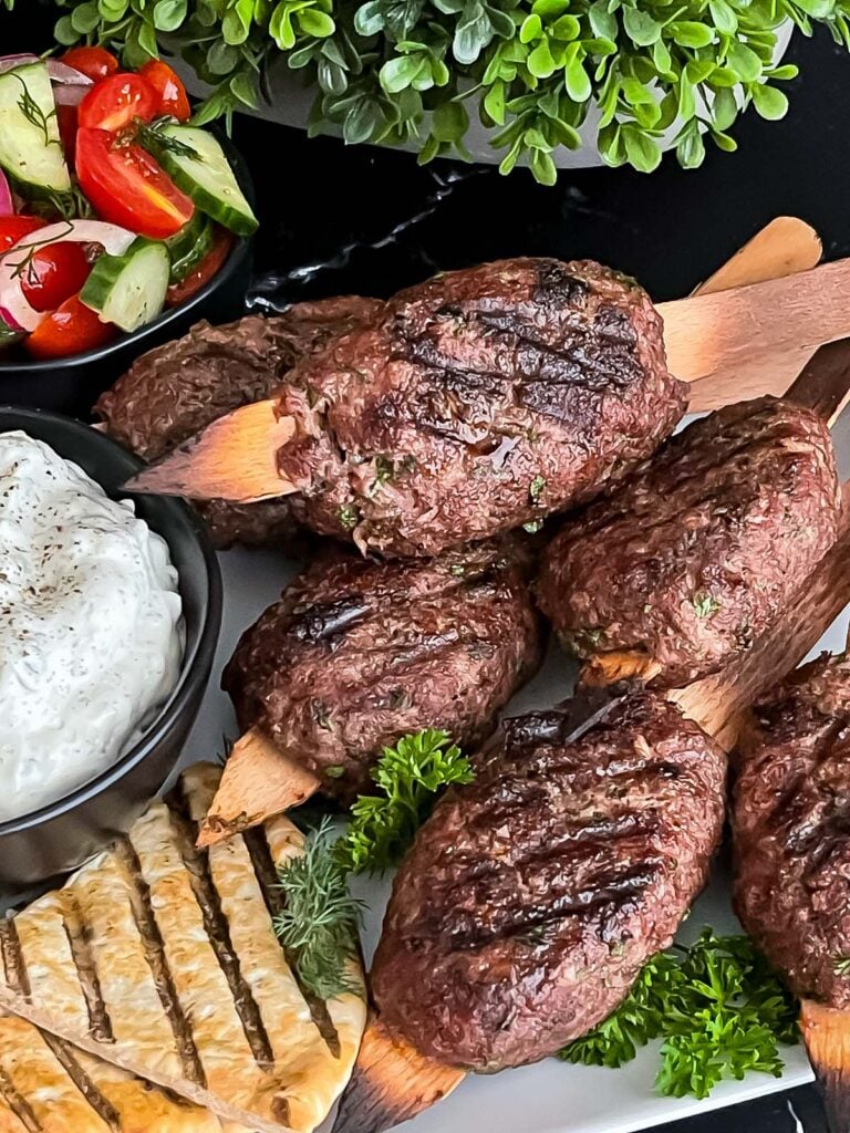 Spiced beef kebabs (kofte) with pita, tzatziki sauce, and a tomato cucumber salad.