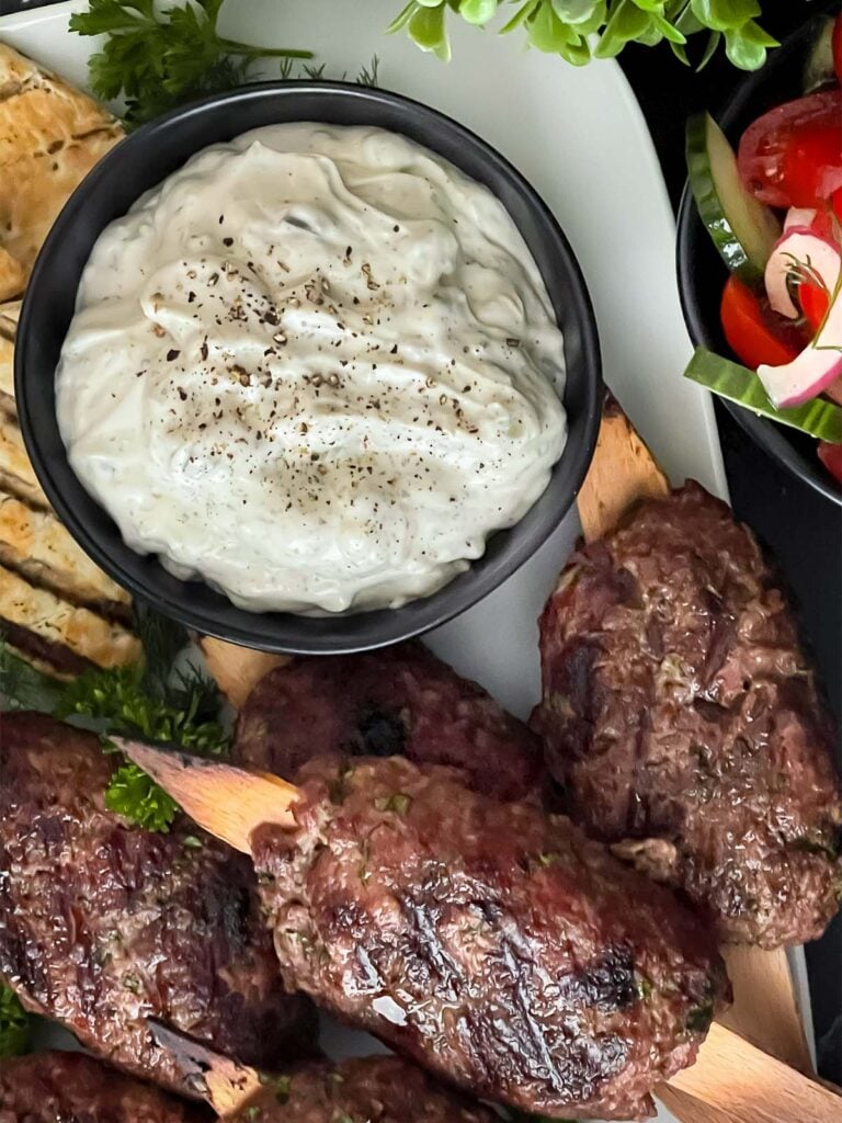 Spiced beef kebabs (kofte) with pita, tzatziki sauce, and a tomato cucumber salad.