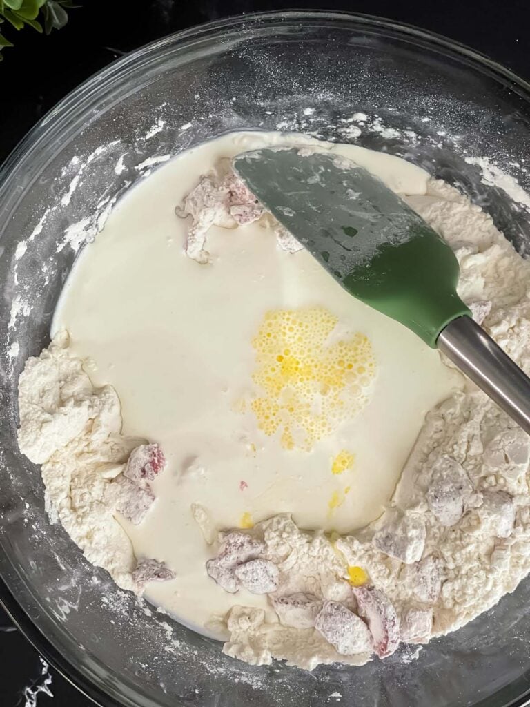 Wet ingredients added to dry ingredients in a glass bowl for strawberry scones.