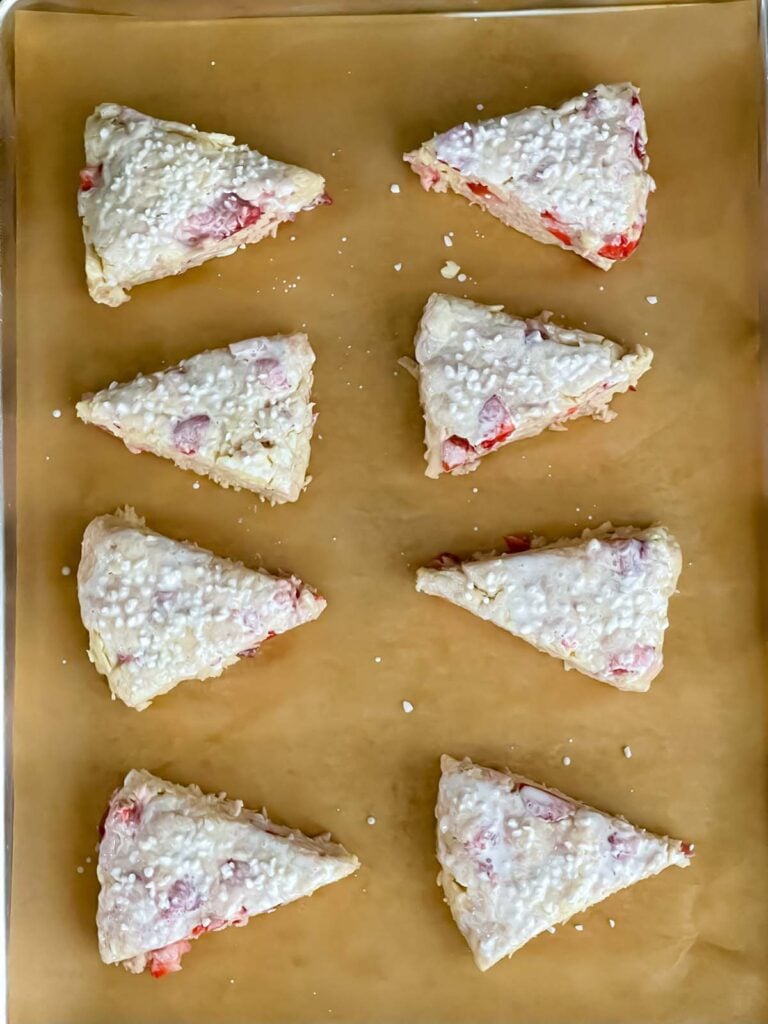 Unbaked strawberry scones topped with heavy cream and coarse sugar.