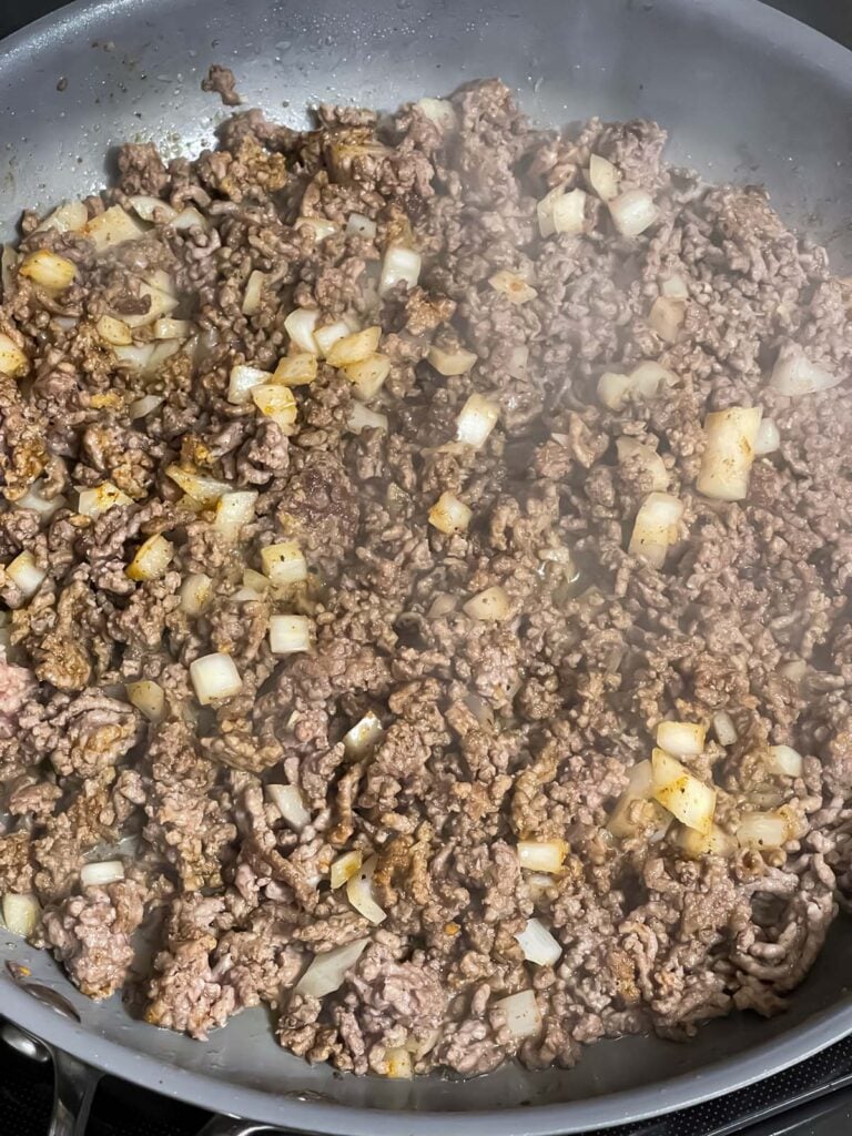 Ground beef, onions, and spices cooking in a skillet.