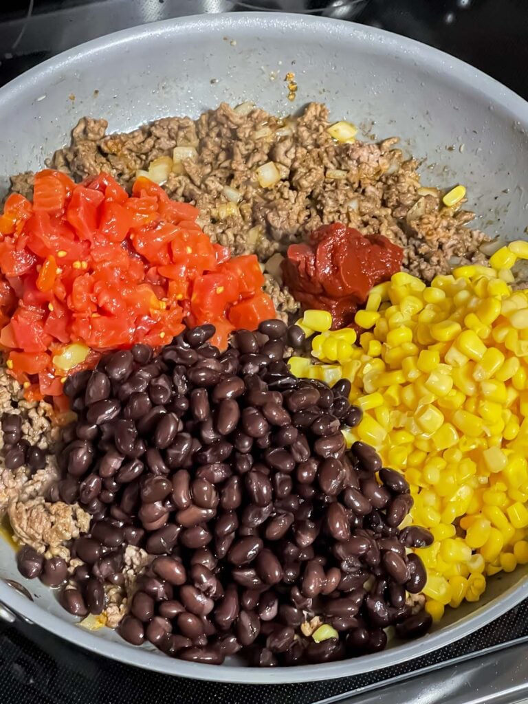 Vegetables added to ground beef in a skillet.