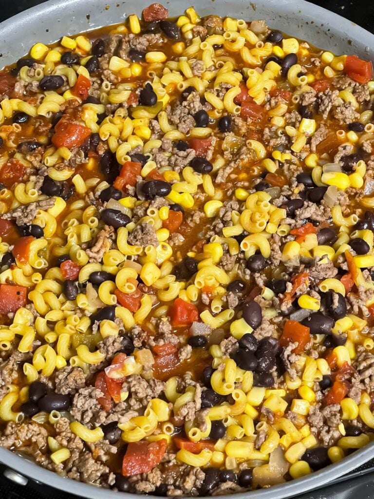 Pasta added to ingredients in a skillet.