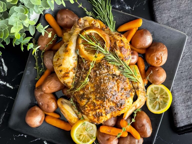 Slow cooker lemon herb whole chicken on a dark plate on a dark surface.