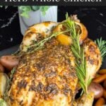 Slow cooker lemon herb whole chicken on a dark plate on a dark surface.