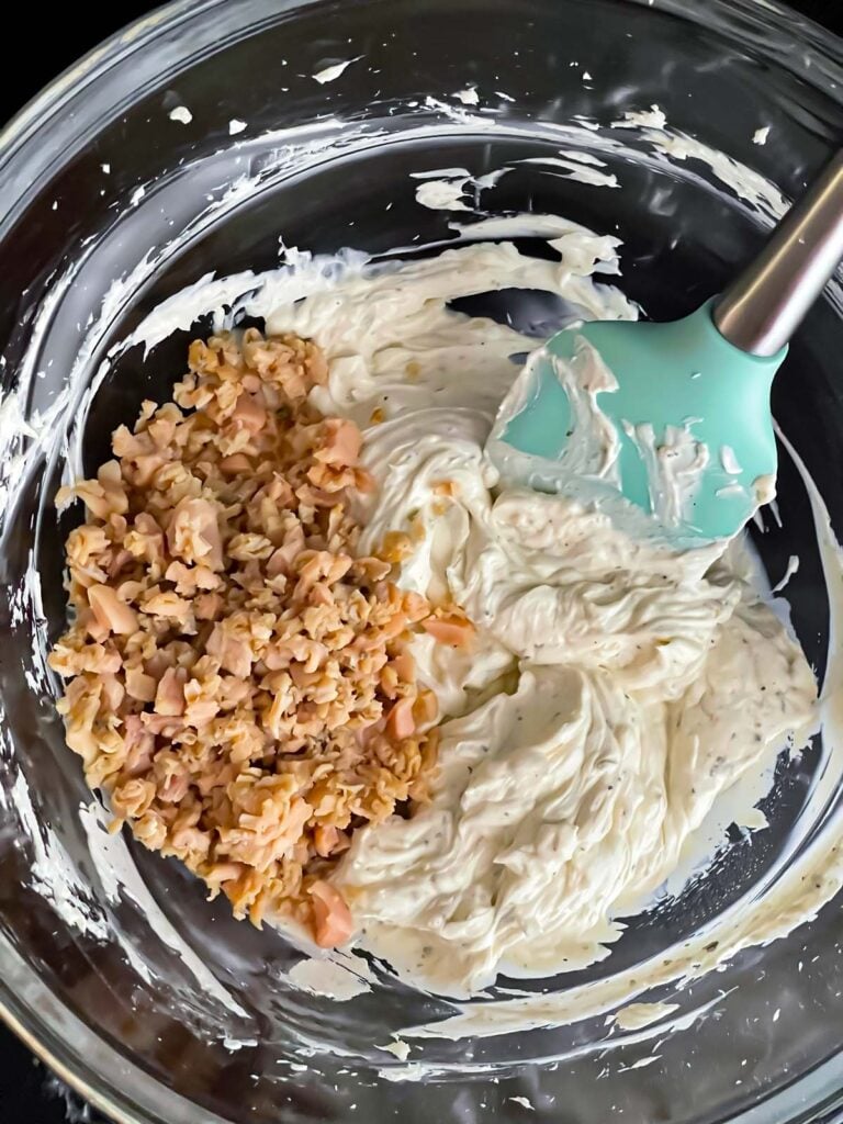 Clam dip ingredients in a glass mixing bowl with the minced clams on top.