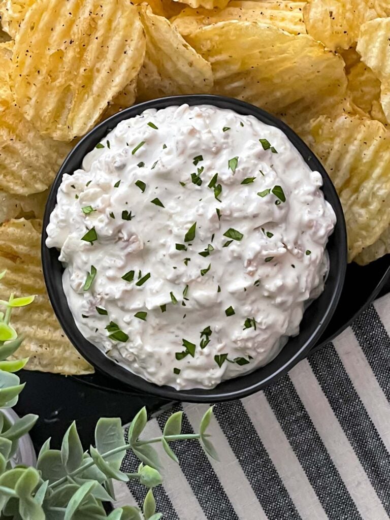 Clam dip in a dark bowl surrounded by kettle potato chips.