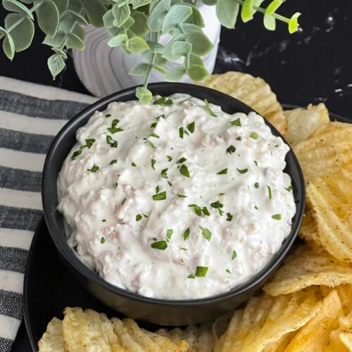 Clam dip in a dark bowl surrounded by kettle potato chips.