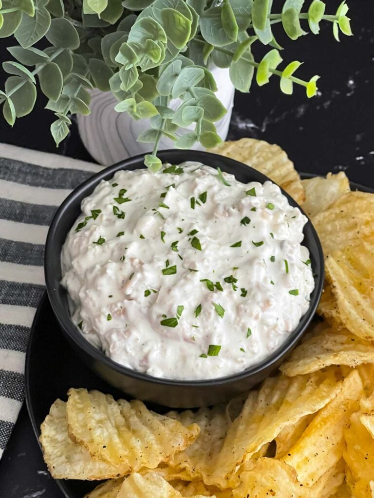 Clam dip in a dark bowl surrounded by kettle potato chips.