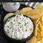 Clam dip in a dark bowl surrounded by kettle potato chips.